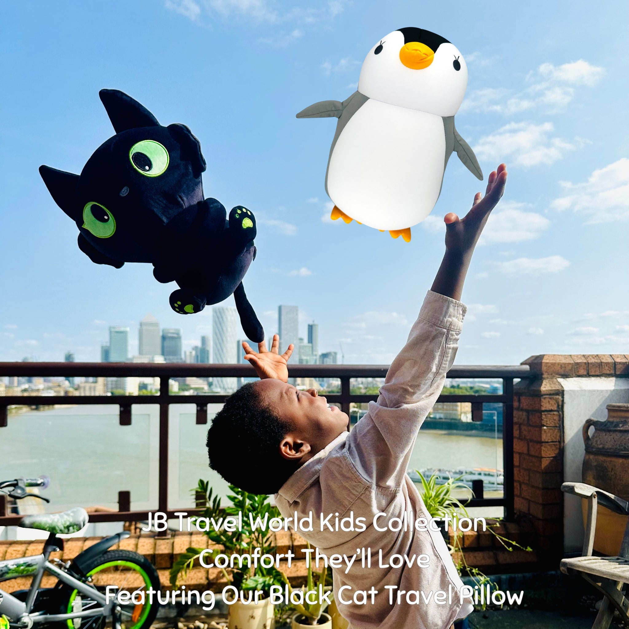 Child playing with a black cat travel pillow and a penguin plush toy against a city skyline.