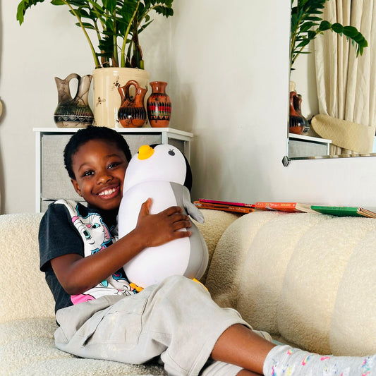Child holding a penguin travel pillow on a couch with decorative vases and plants in the background