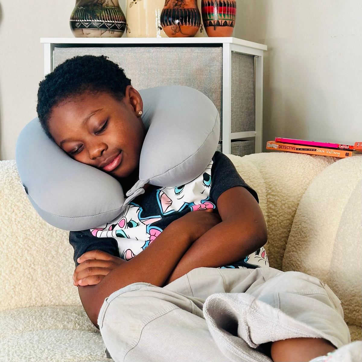 A child resting on a sofa using the JB Travel World plush penguin 2-in-1 travel pillow as a U-shaped neck pillow.