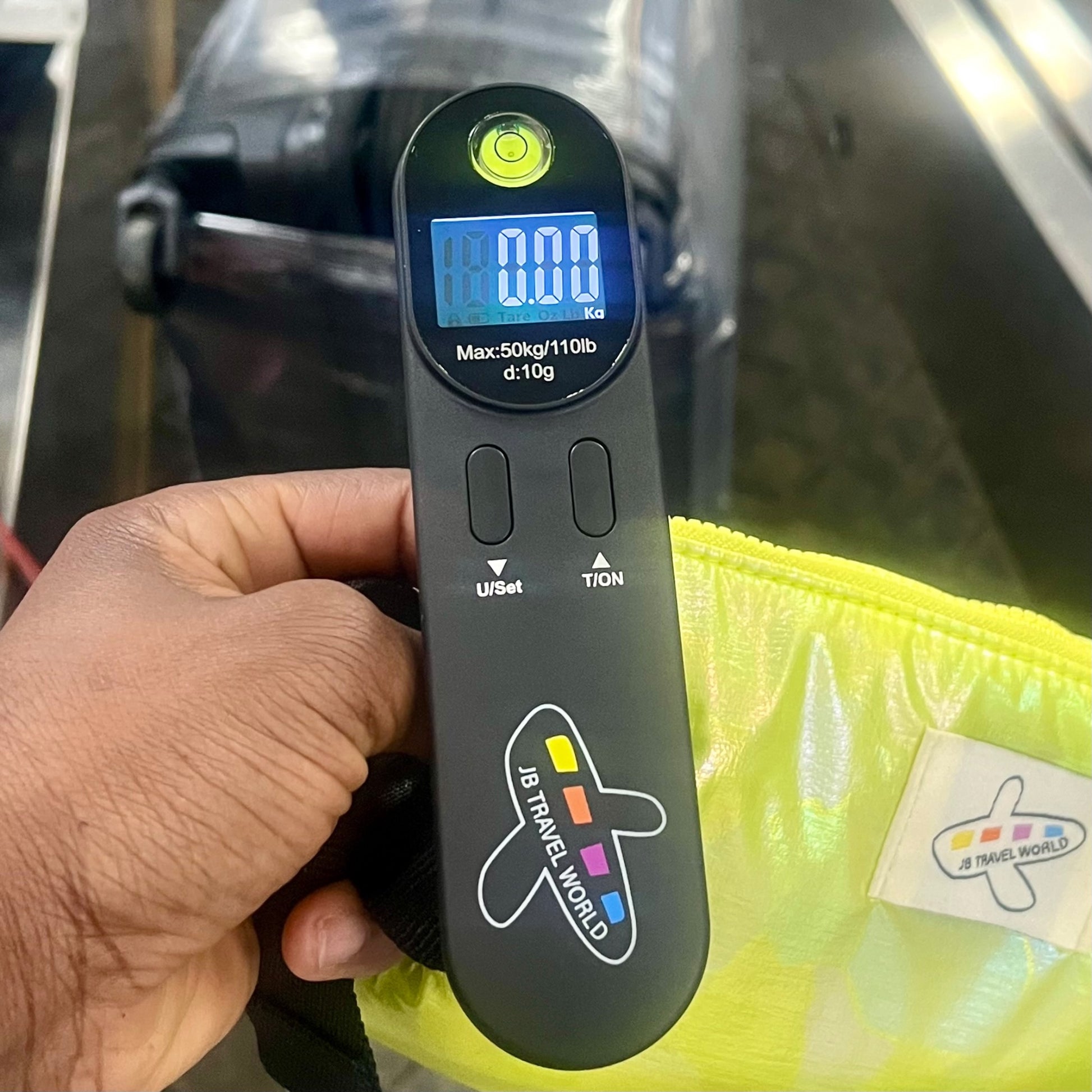 Digital luggage scale held by a hand with a green iridescent travel bag in the background