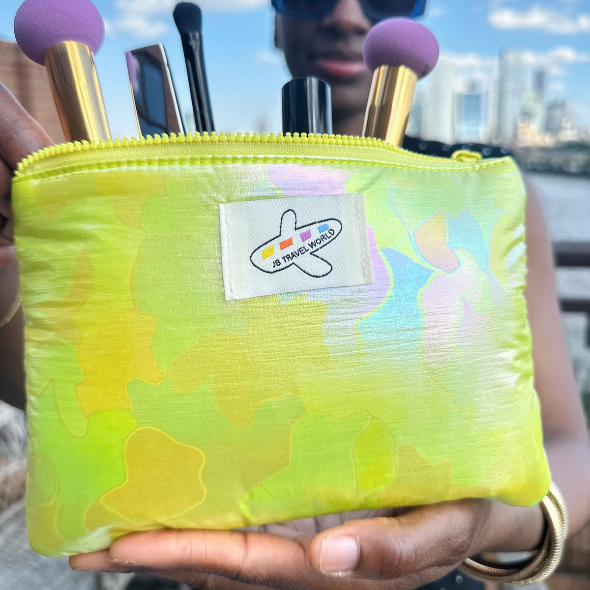 Green shimmer cosmetic bag held open displaying brushes and makeup – travel essentials set